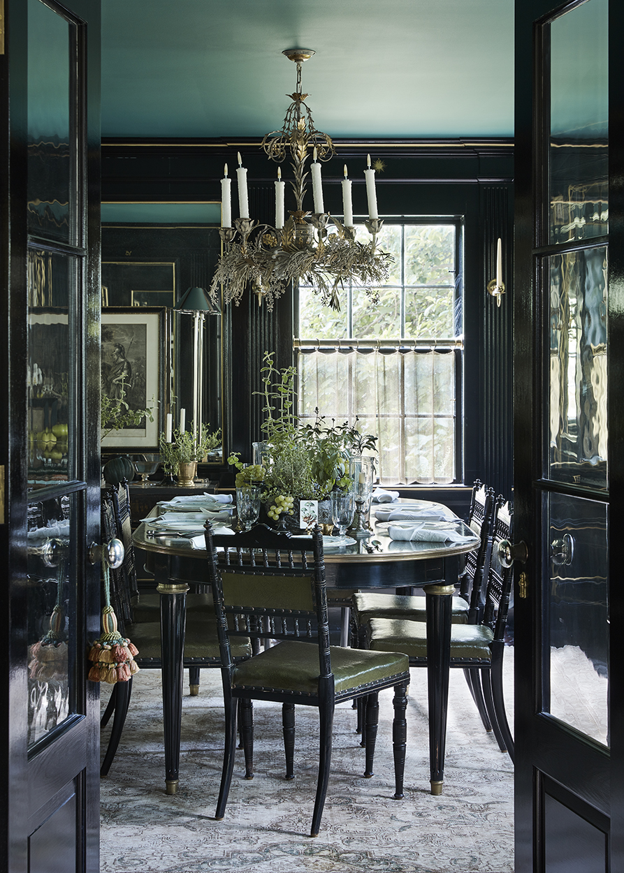 Formal dining room interior with black walls, an oval table set for dinner, upholstered chairs, and a decorative chandelier.