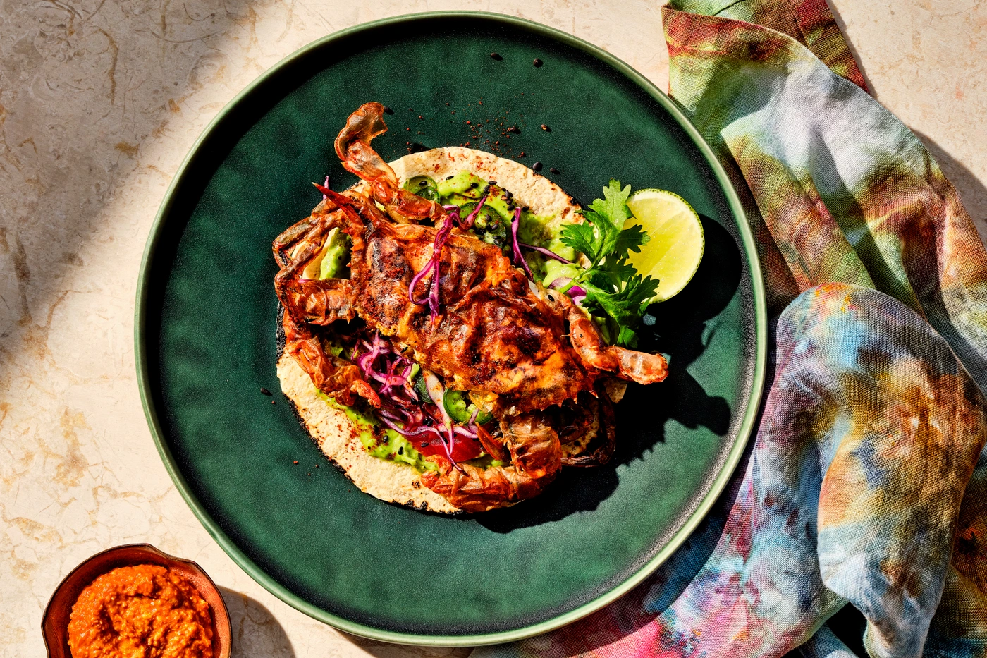 Soft shell crab taco on a deep green ceramic plate with lime wedge, herbs, and a tie-dye napkin