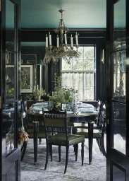 View through dark double doors into an elegant dining room styled by Sophie Strangio with a dark table, chandelier, and green accents