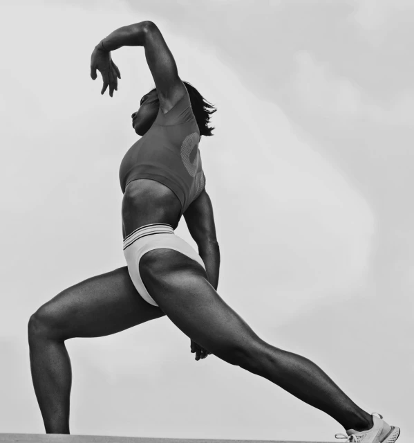 Athletic woman in sportswear in a dynamic pose against a bright cloudy background. Full-body shot showcasing strength and flexibility outdoors.