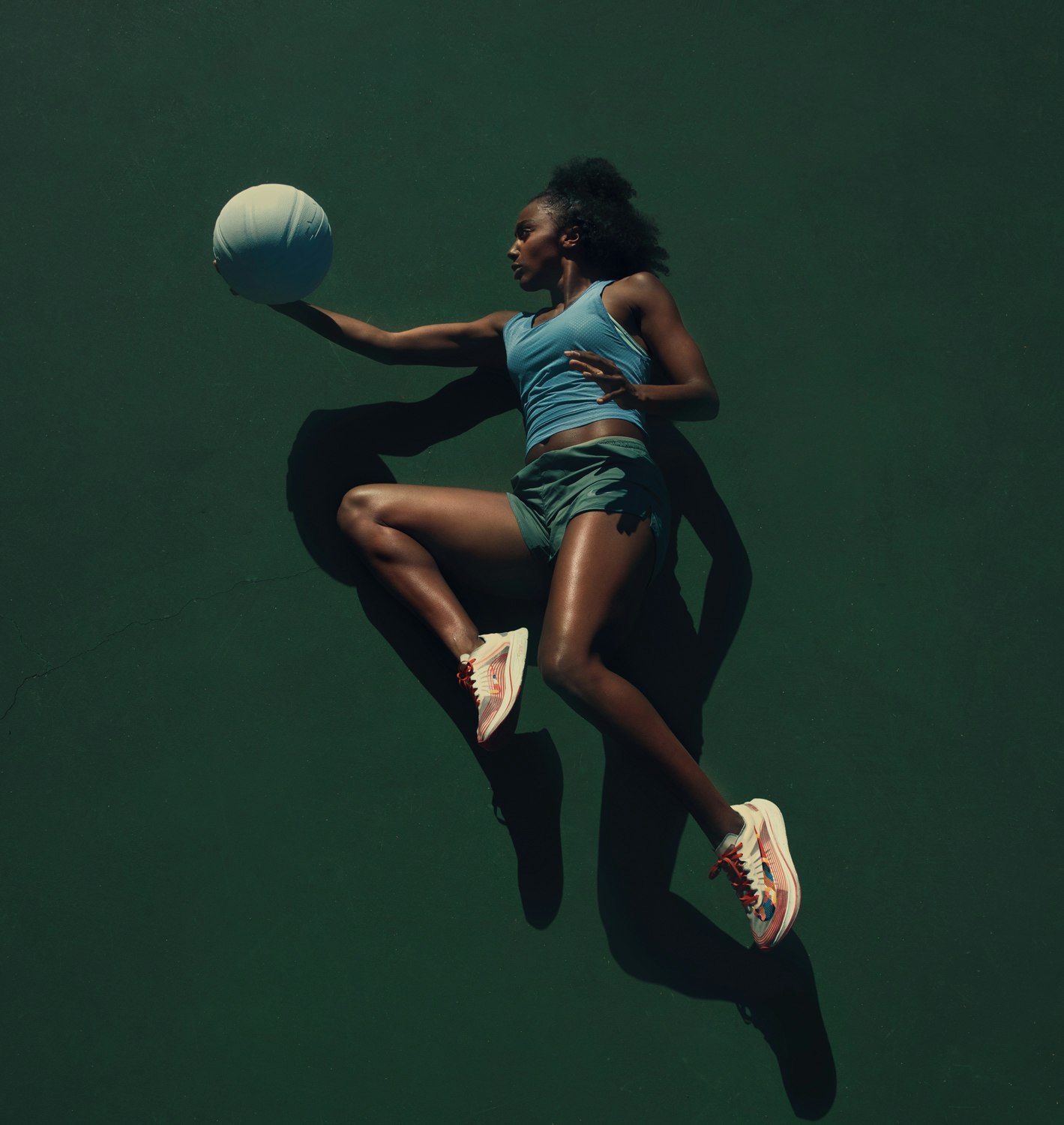 Athletic woman jumps with a white basketball against a dark green backdrop, illuminated by studio lighting, showcasing a dynamic sports scene.