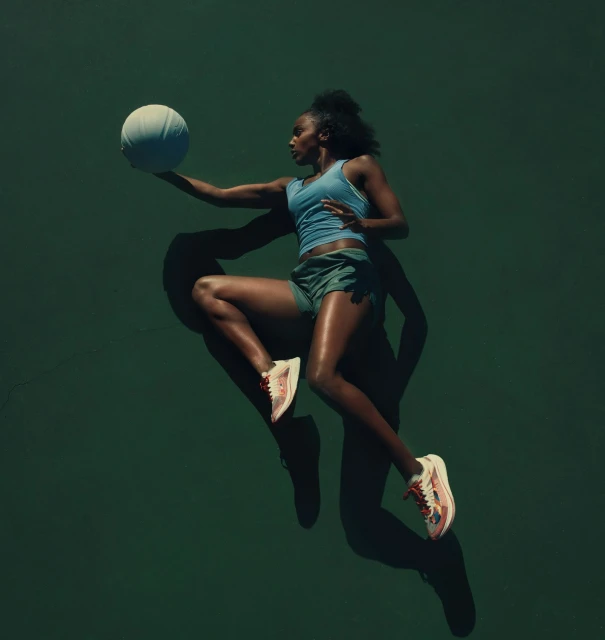 Athletic woman jumps with a white basketball against a dark green backdrop, illuminated by studio lighting, showcasing a dynamic sports scene.