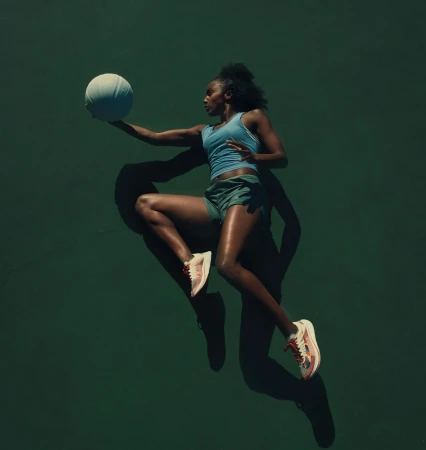 Athletic woman jumps with a white basketball against a dark green backdrop, illuminated by studio lighting, showcasing a dynamic sports scene.
