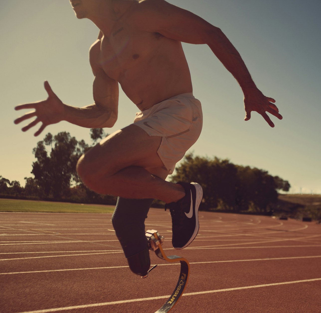 Male athlete with a prosthetic leg runs on an outdoor track under a clear sky, showcasing fitness, sports, and determination.