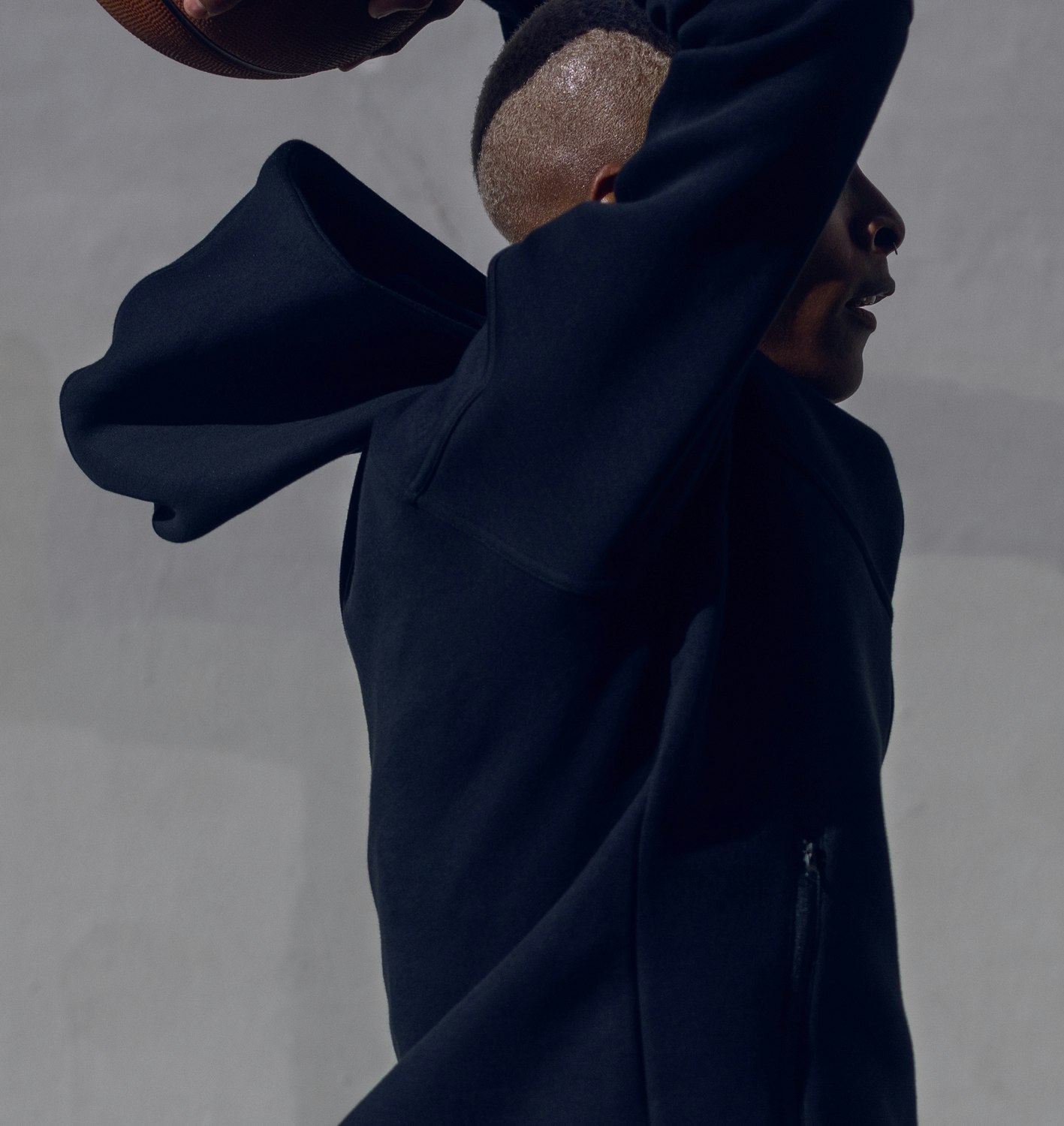 Athletic Black man in mid-air reaching for a basketball in a studio setting, wearing a navy hoodie and captured in a medium shot.