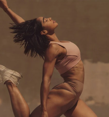 Athletic woman in sportswear leaping with outstretched arm against a neutral background, showcasing fitness and active lifestyle in motion.
