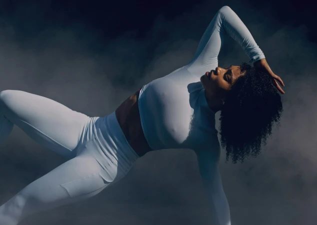 Dancer in white activewear posing dynamically amidst dark smoke captured by Brian Lowe.