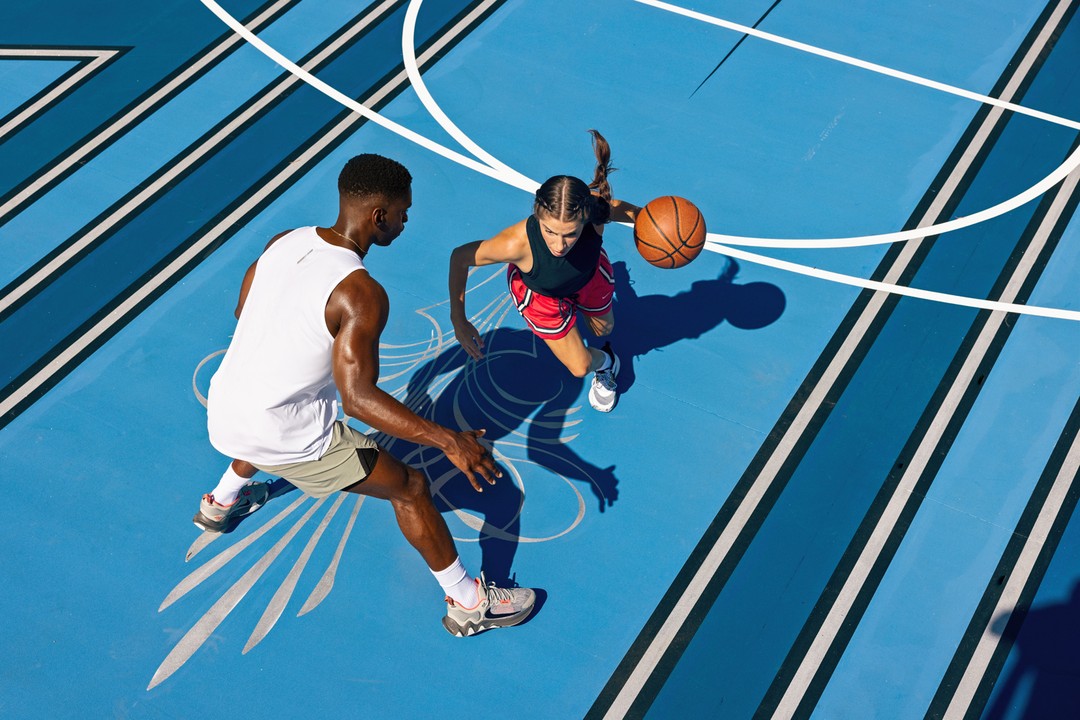 High-angle shot on blue basketball court featuring a man and woman playing basketball on a sunny day, highlighting sports and fitness.