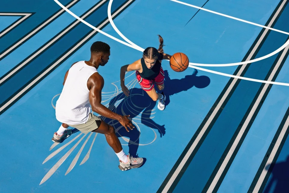 High-angle shot on blue basketball court featuring a man and woman playing basketball on a sunny day, highlighting sports and fitness.