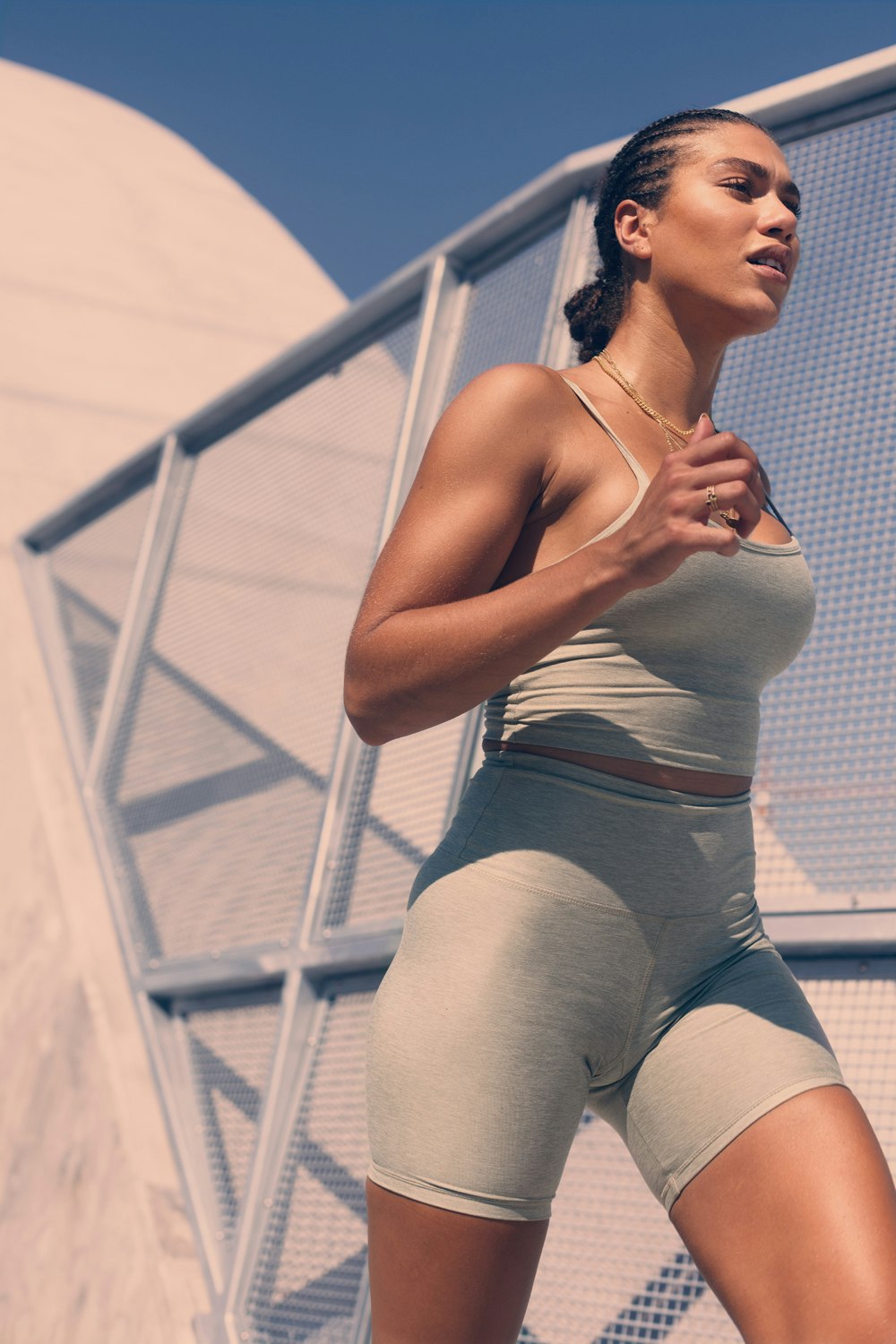 Athletic woman in activewear poses outdoors in sunlight. Braids, tank top, and shorts. Fitness and healthy lifestyle concept.
