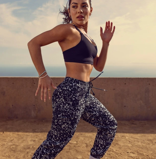 Athletic woman running outdoors, wearing a black sports bra and patterned pants, captured in a medium shot with soft, natural lighting.