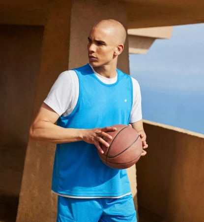 Bald man wearing blue basketball jersey and white t-shirt holding basketball outdoors
