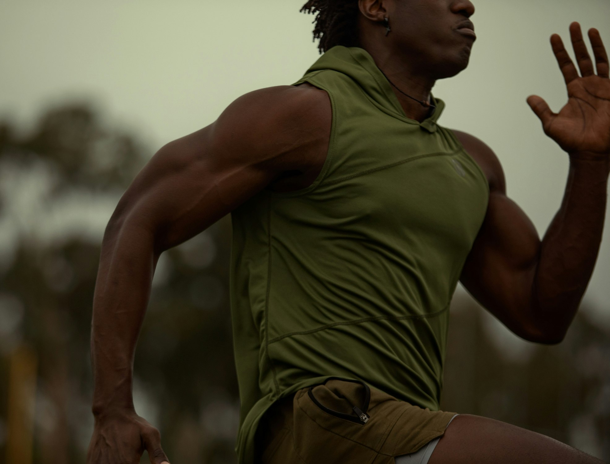 Muscular African-American man in athletic wear running outdoors, showcasing arm muscles and fitness in an action shot.