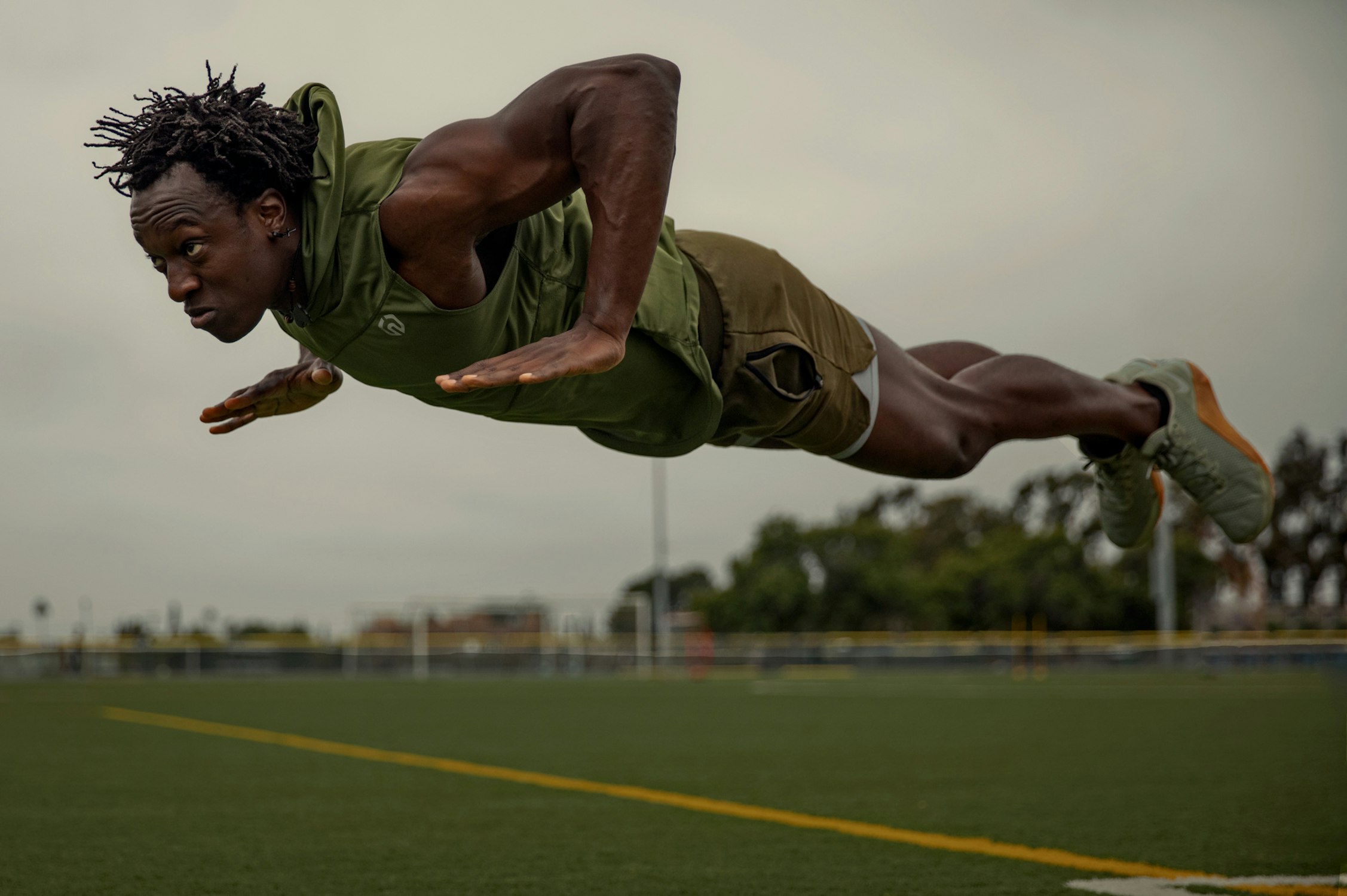 Muscular man in athletic gear performing push-ups outdoors on a green field under a cloudy sky; fitness, health, exercise, strength.