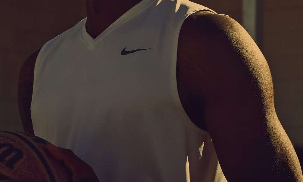 Athletic man holding a Wilson basketball close-up shot in a white Nike sleeveless shirt, showcasing fitness and sports branding.