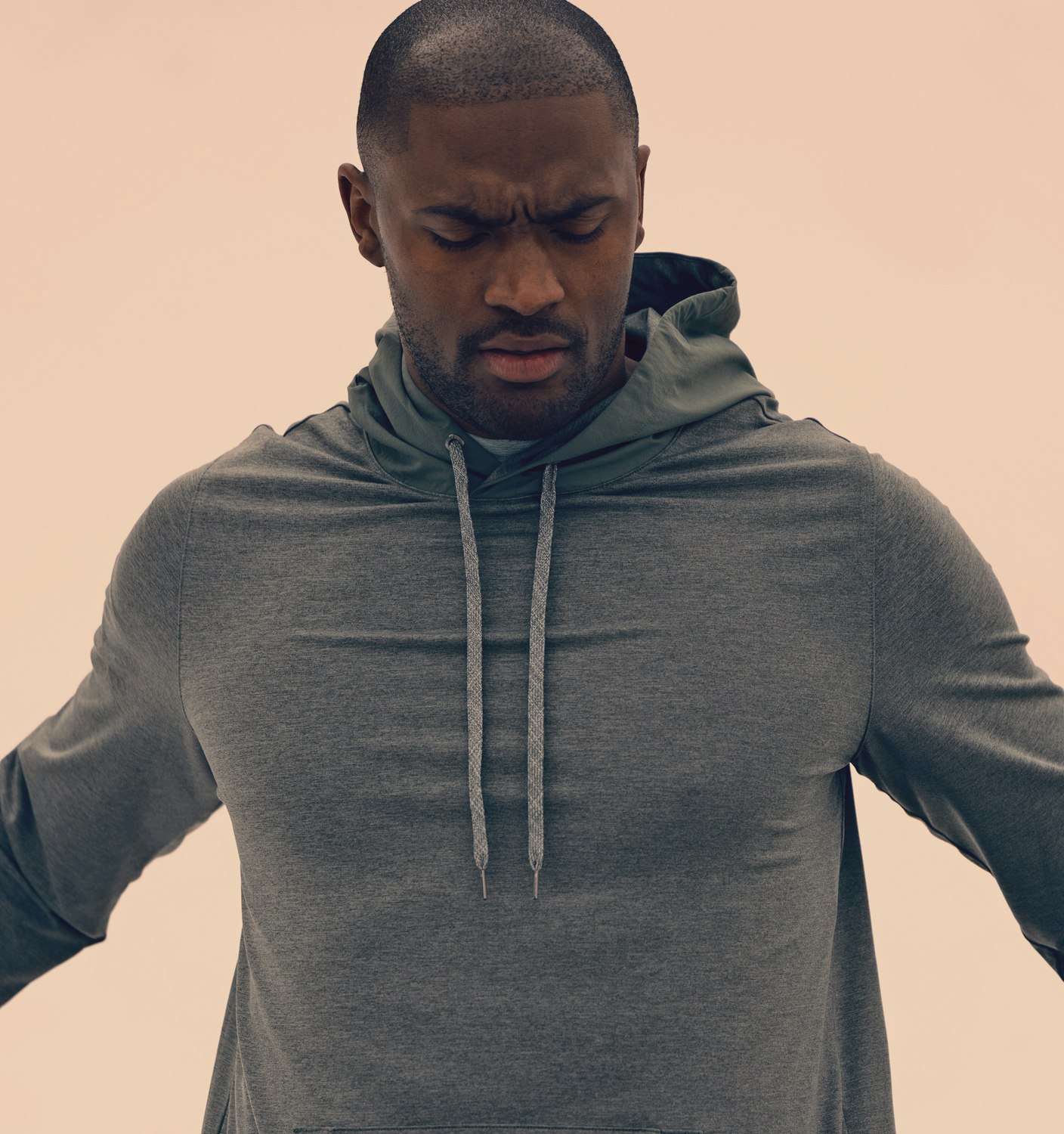 Close-up of an adult Black man with a concerned expression, wearing a gray hooded sweatshirt against a peach-colored backdrop.