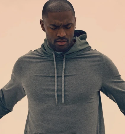 Close-up of an adult Black man with a concerned expression, wearing a gray hooded sweatshirt against a peach-colored backdrop.