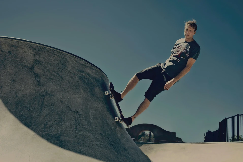 Skateboarder performs a trick on a concrete ramp in a skatepark under a clear blue sky, showcasing action and athleticism.