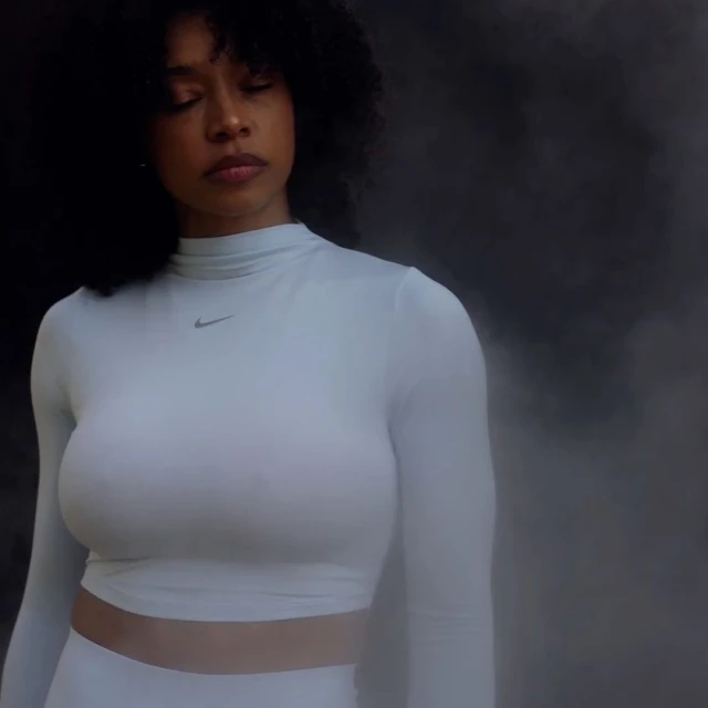 Woman in long-sleeved shirt poses against a dark background, eyes closed, showcasing fashion and portrait photography.