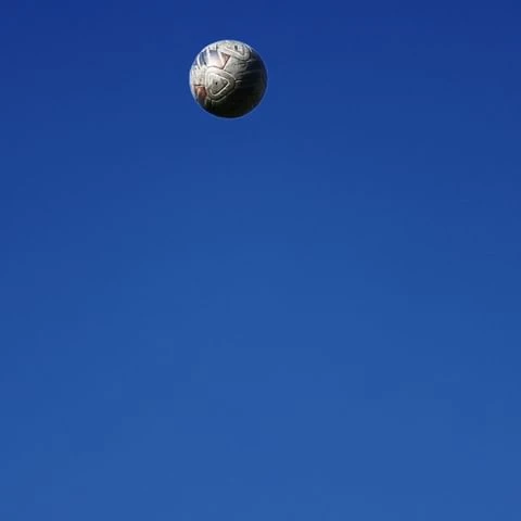 A white soccer ball is suspended in a clear blue sky with no clouds, creating a minimalist and sporty composition.
