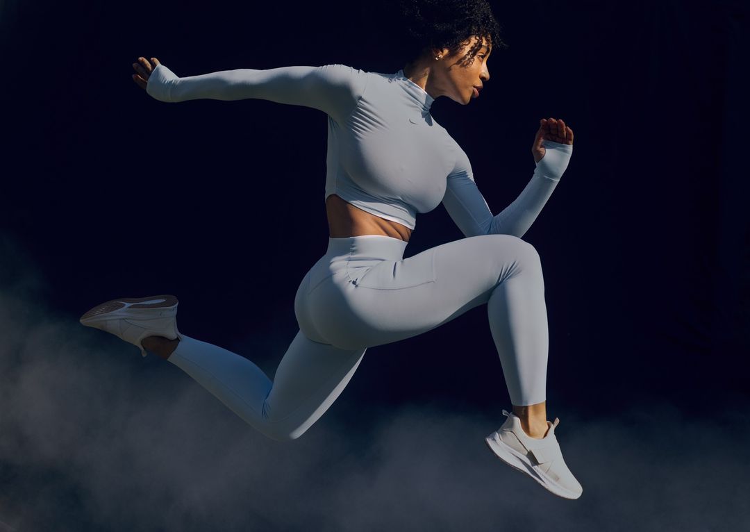 Athletic woman in light-blue athletic wear jumps in a dark studio setting. Activewear and fitness concept, action shot.