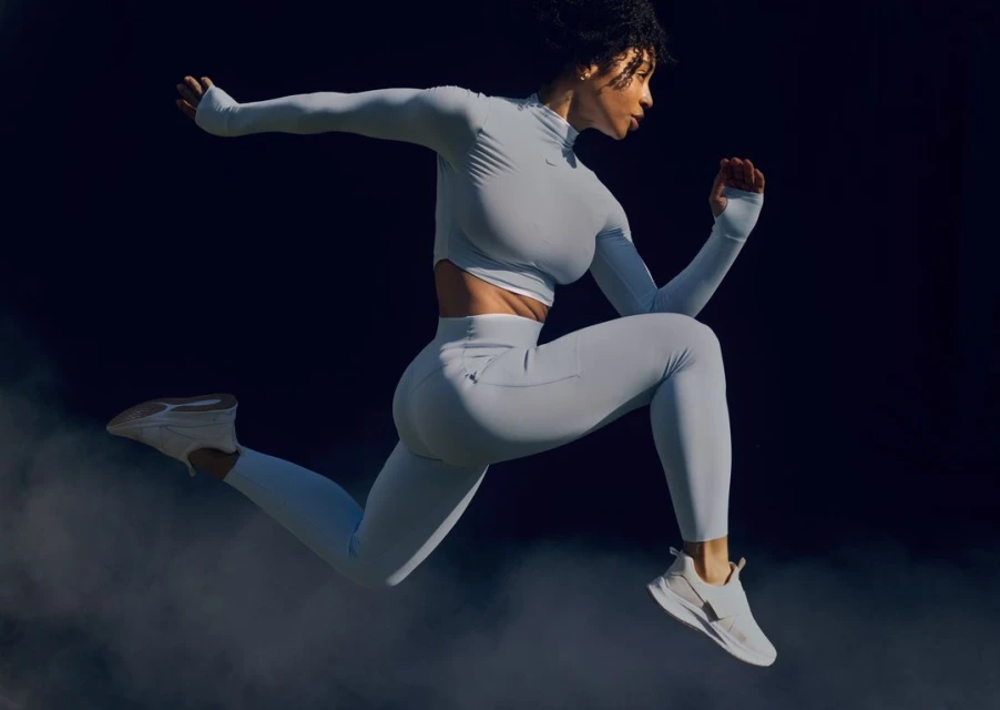 Athletic woman in light-blue athletic wear jumps in a dark studio setting. Activewear and fitness concept, action shot.
