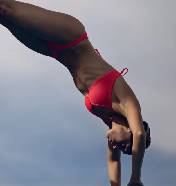 Athletic woman diving gracefully in a red bikini against a bright, clear sky showcasing athleticism and summer vibes. 