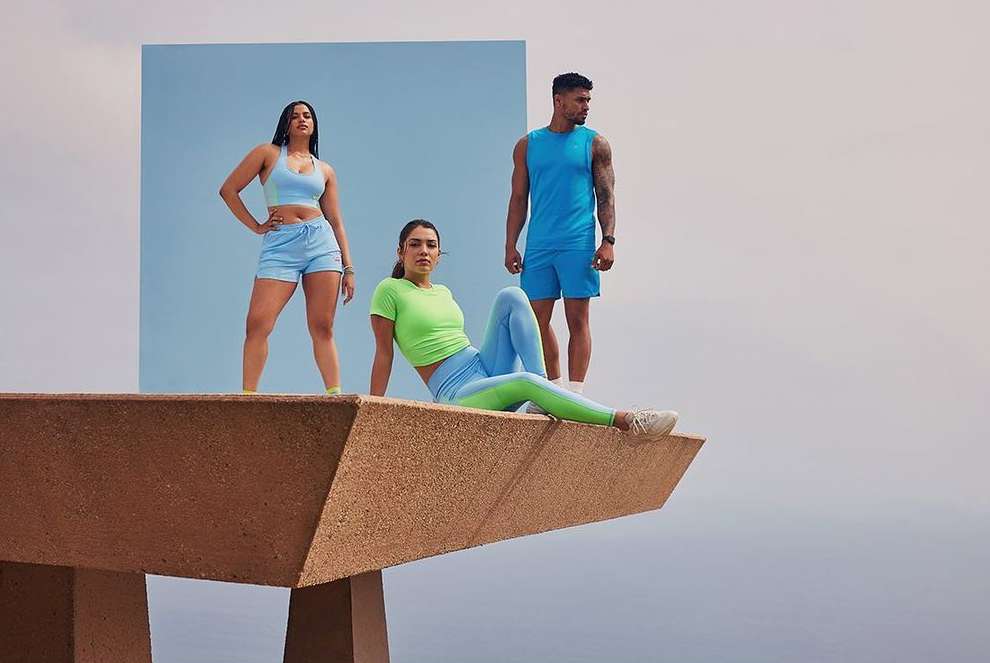 Three athletic adults in sportswear posing on a geometric platform against a split blue and white backdrop, fitness fashion concept.
