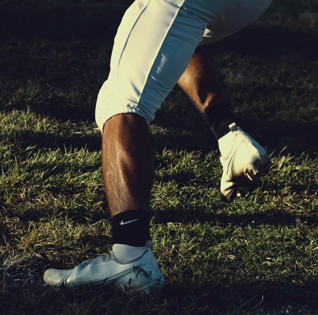 Legs of a football player in white pants and cleats on a grassy field, highlighting athletic apparel and outdoor sport in daylight.