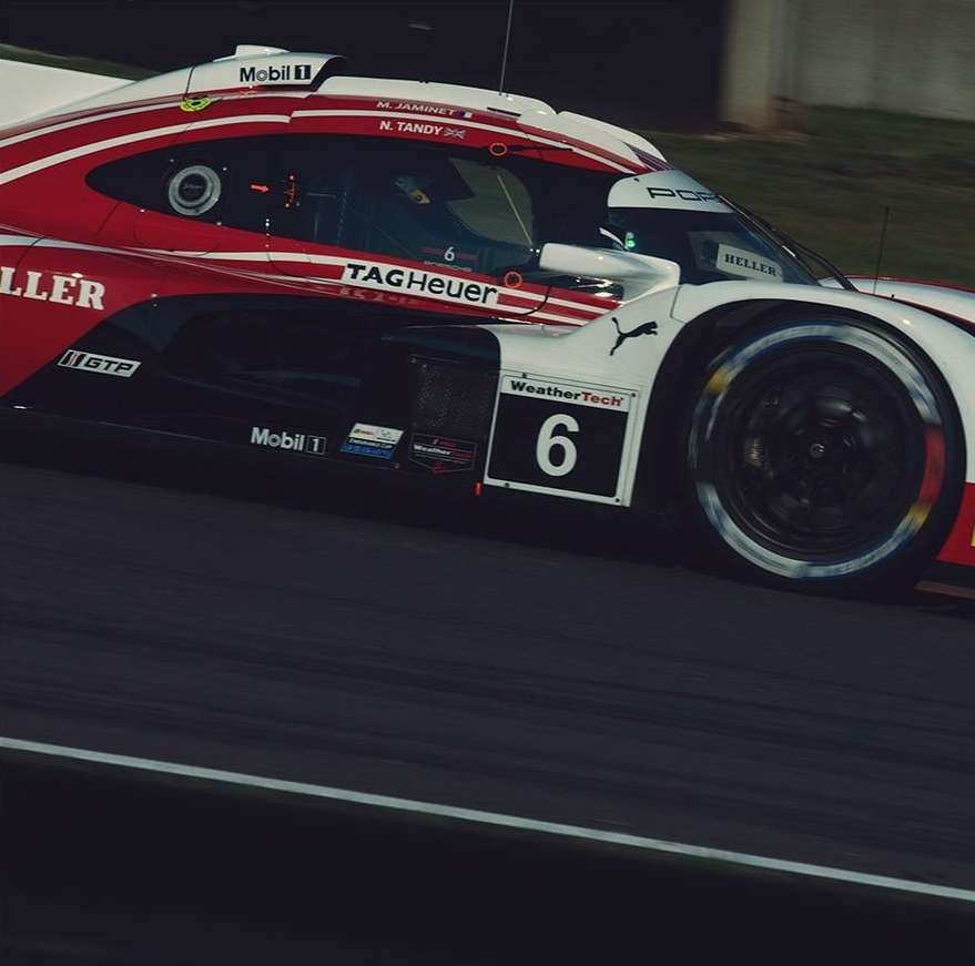 Red and white Porsche race car speeds on a grey track during daytime, capturing the thrill of motorsport racing.