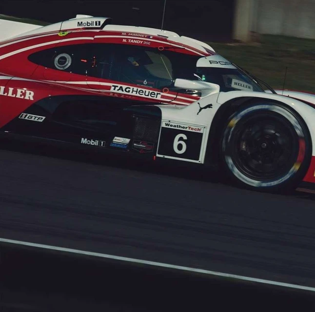 Red and white Porsche race car speeds on a grey track during daytime, capturing the thrill of motorsport racing.