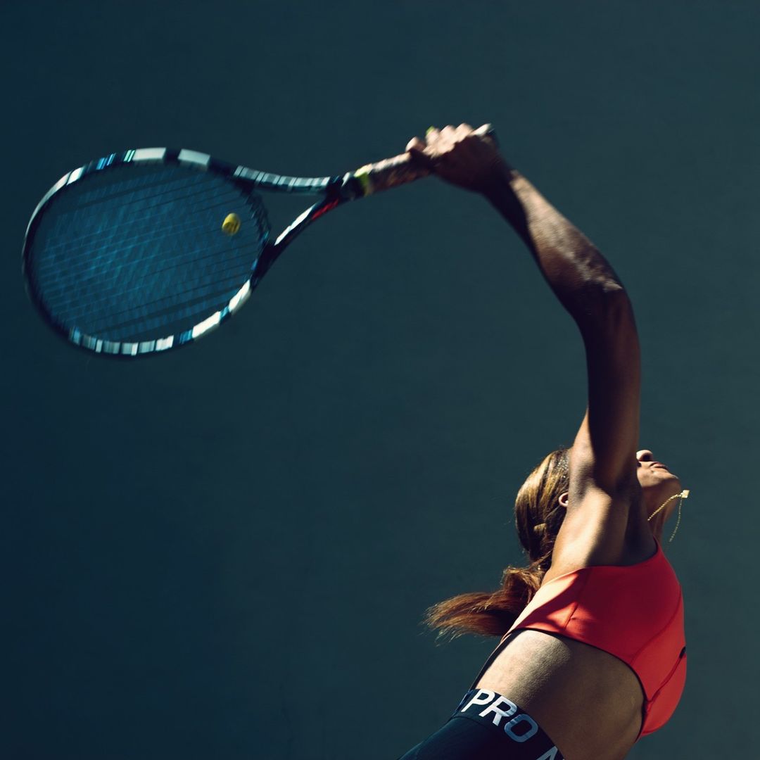 Action shot of a woman serving during a tennis match, showcasing her athletic pose, equipment, and sportswear.