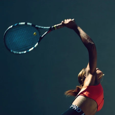 Action shot of a woman serving during a tennis match, showcasing her athletic pose, equipment, and sportswear.