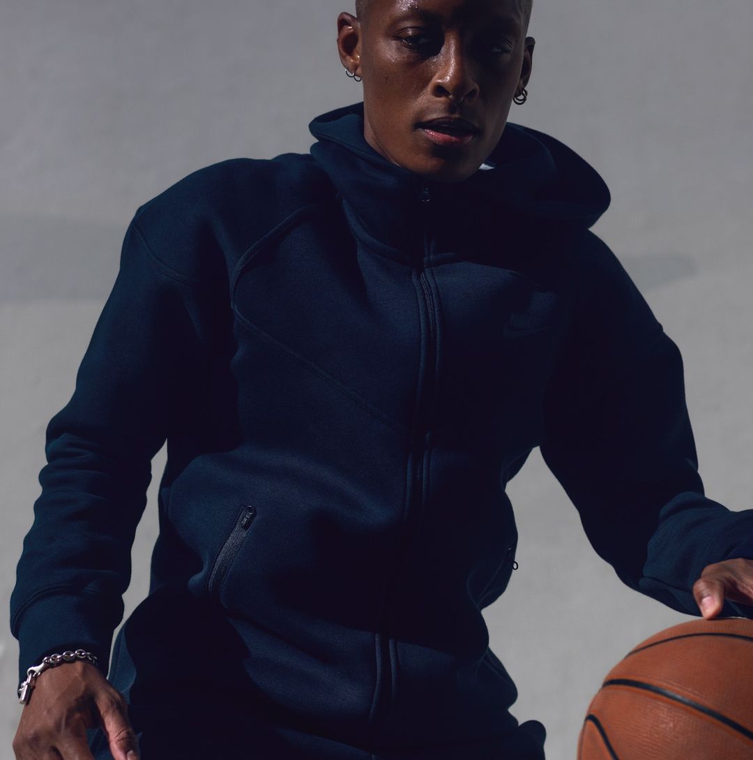 Athletic Black man in dark blue sportswear dribbles a basketball against a neutral backdrop in an active sports setting indoors.