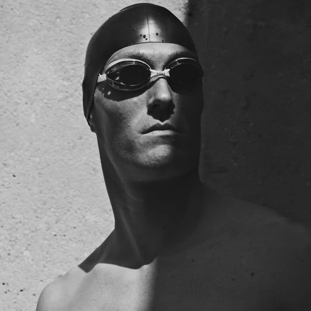 Black and white portrait of a swimmer with a cap and goggles, strong light and shadow.
