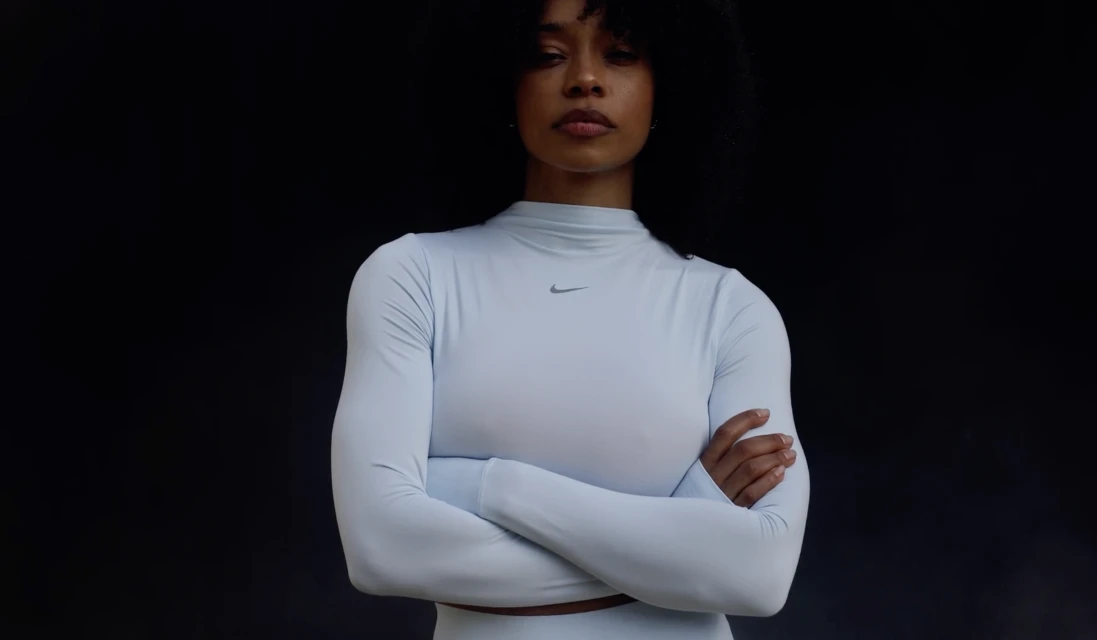 Athletic woman with arms crossed in light blue long-sleeve activewear top in a studio, showcasing sportswear fashion against dark backdrop.