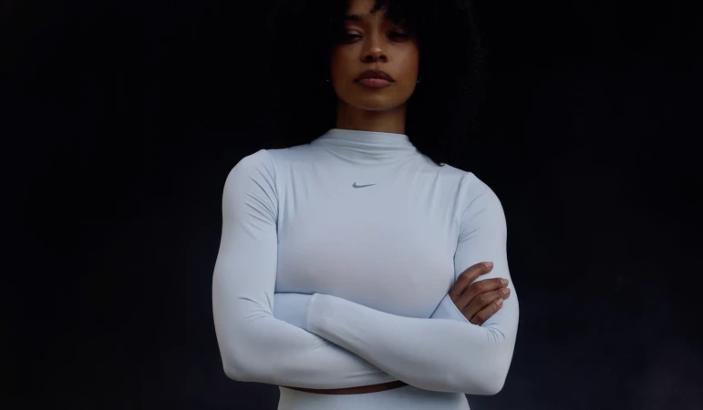 Athletic woman with arms crossed in light blue long-sleeve activewear top in a studio, showcasing sportswear fashion against dark backdrop.