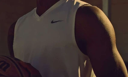 Close-up of a black man wearing a white sports tank top holding a basketball under warm lighting by Brian Lowe