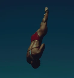 A diver in a red swimsuit plunging downwards through deep blue water captured by Brian Lowe