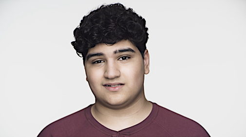 Portrait of a young man with dark, curly hair, wearing a burgundy top, set against a bright white background in a studio setting.