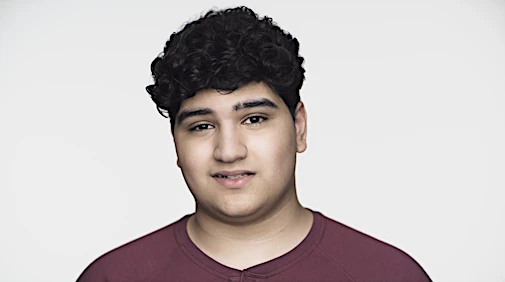 Portrait of a young man with dark, curly hair, wearing a burgundy top, set against a bright white background in a studio setting.