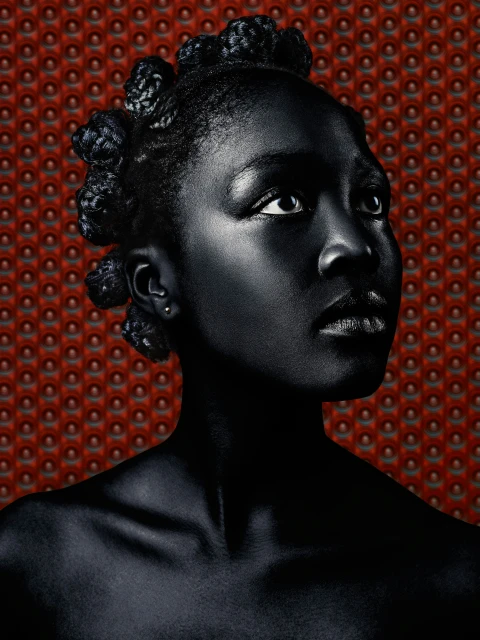 Portrait of an adult Black woman with stylized coiled hair, gazing upwards with a red patterned background in an indoor environment.