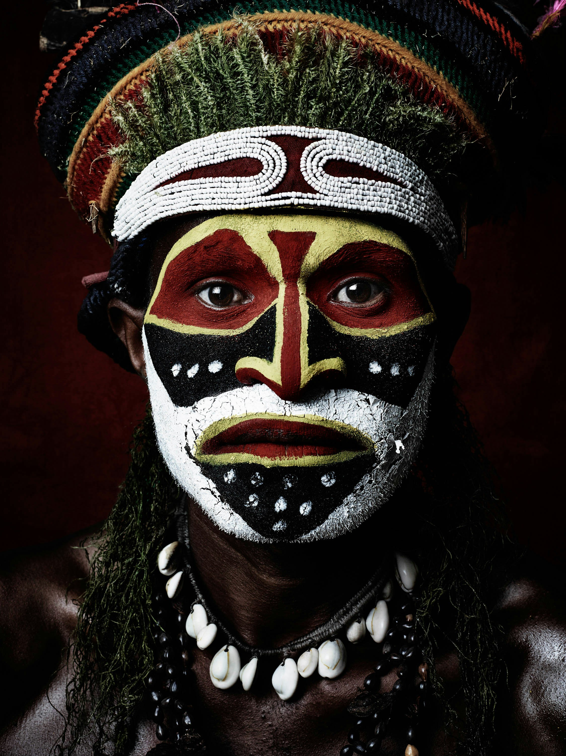 Striking close-up portrait of a man with elaborate face paint and a decorative headdress, showcasing cultural attire and artistic expression.