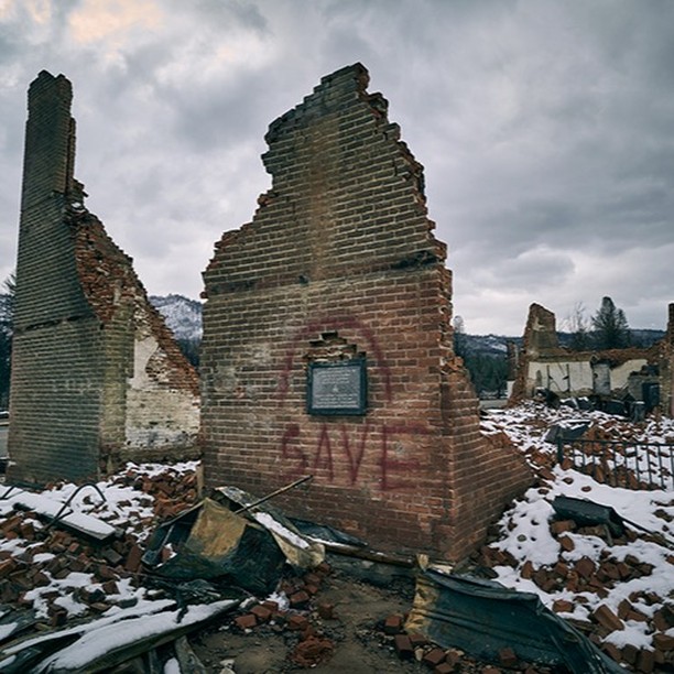 Ruins of a brick building under a cloudy sky, with remnants of snow and debris scattered around the site and surrounding landscape.