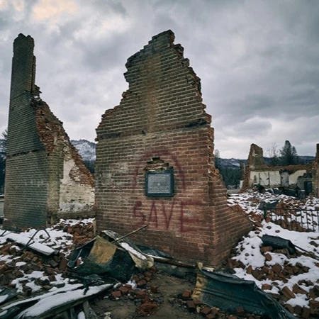 Ruins of a brick building under a cloudy sky, with remnants of snow and debris scattered around the site and surrounding landscape.