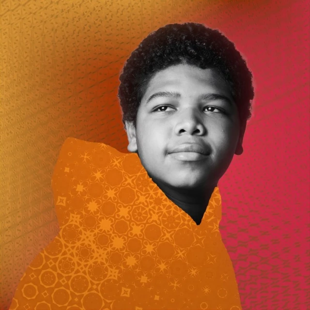 Black and white portrait of a boy with an afro, wearing an orange hooded sweatshirt with a patterned design over a colorful background.
