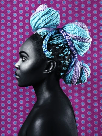 Profile portrait of a young Black woman with braided turquoise and purple hair styled in buns against a purple polka dot backdrop.