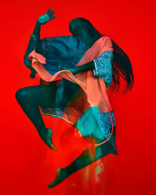 Fashion shot of a woman in motion with dark skin and flowing black hair. She wears a peach colored top, on a bright red backdrop.