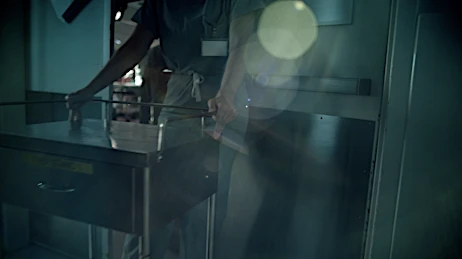 Medical professional in scrubs opens a stainless steel medical cart in a dimly lit healthcare setting, with lens flare.