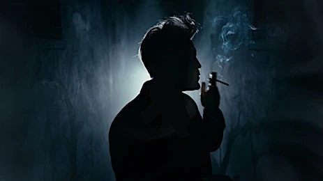 Silhouette of a person smoking a cigarette against a dark background with smoke, creating a moody and atmospheric visual.